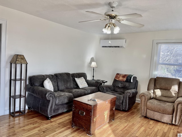 living room with light wood-style flooring, a textured ceiling, a ceiling fan, and a wall mounted air conditioner