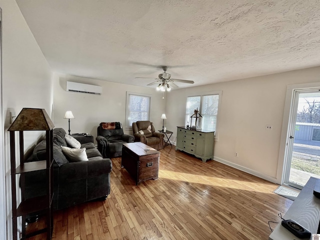 living room with a textured ceiling, an AC wall unit, hardwood / wood-style flooring, and baseboards