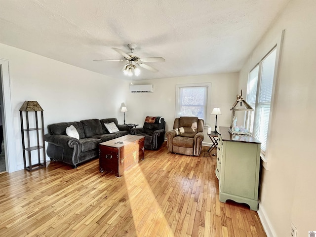 living area with light wood-style floors, ceiling fan, a textured ceiling, and a wall mounted AC