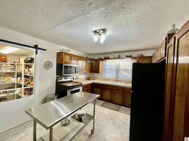 kitchen with electric stove, stainless steel microwave, a barn door, freestanding refrigerator, and a sink