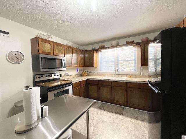 kitchen with tile countertops, appliances with stainless steel finishes, a textured ceiling, and a sink