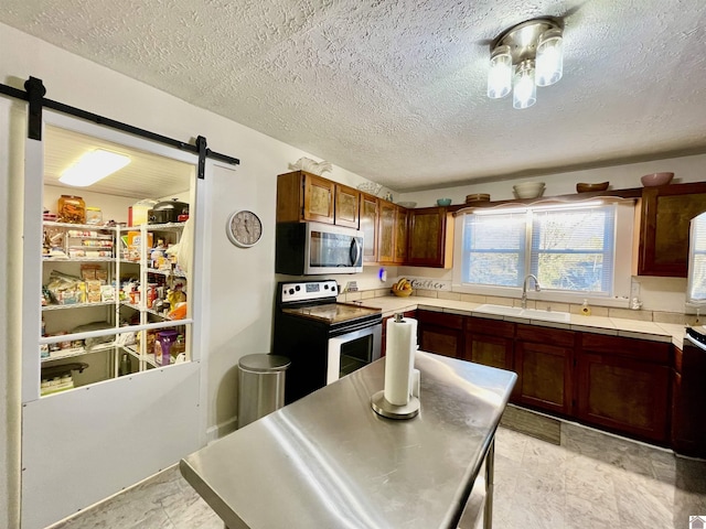 kitchen with a barn door, range with electric cooktop, a sink, tile counters, and stainless steel microwave