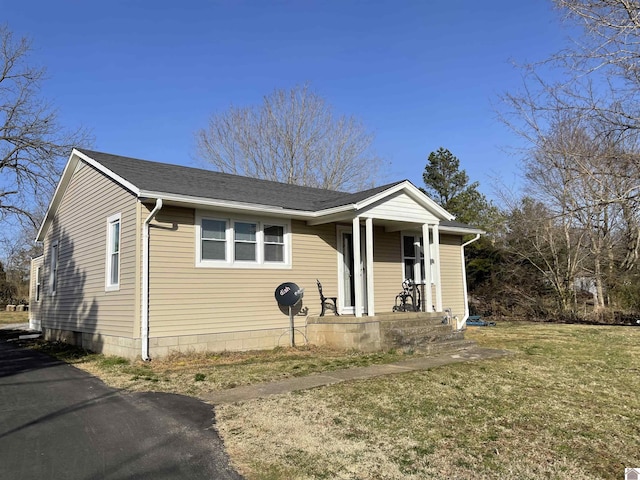 bungalow-style home featuring covered porch, a front lawn, and roof with shingles