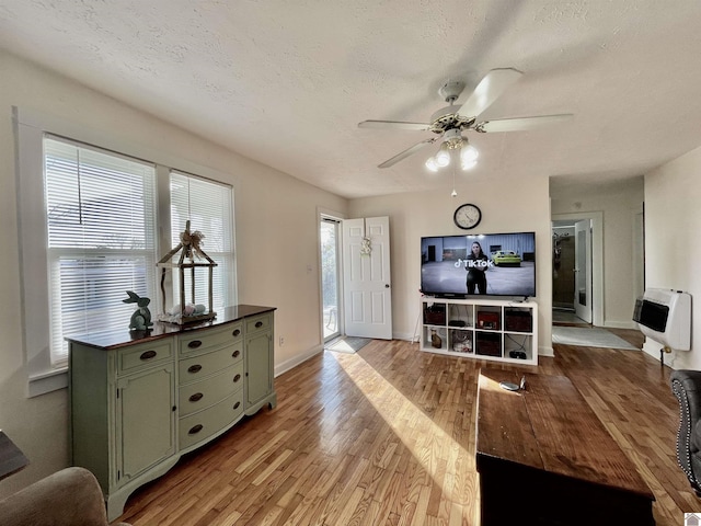 living area with heating unit, a textured ceiling, a ceiling fan, and wood finished floors