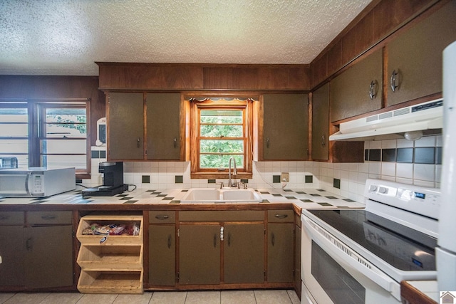 kitchen featuring a sink, under cabinet range hood, white appliances, decorative backsplash, and tile counters