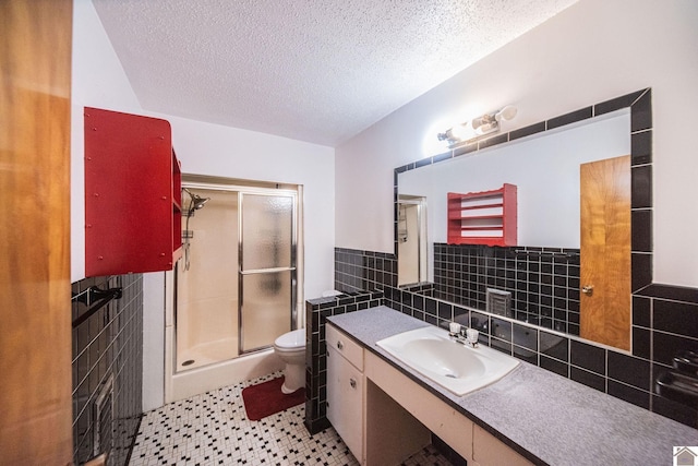 bathroom featuring a wainscoted wall, toilet, a textured ceiling, tile walls, and a shower stall