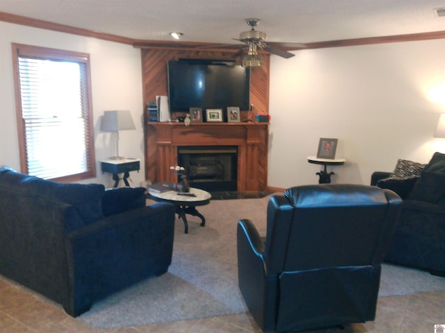 living area with a ceiling fan, a glass covered fireplace, crown molding, and tile patterned flooring