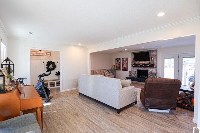 living area featuring baseboards, visible vents, light wood-style flooring, a fireplace, and ornamental molding