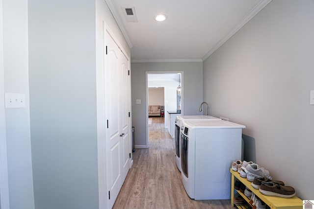 clothes washing area featuring visible vents, ornamental molding, light wood-style flooring, laundry area, and washing machine and clothes dryer