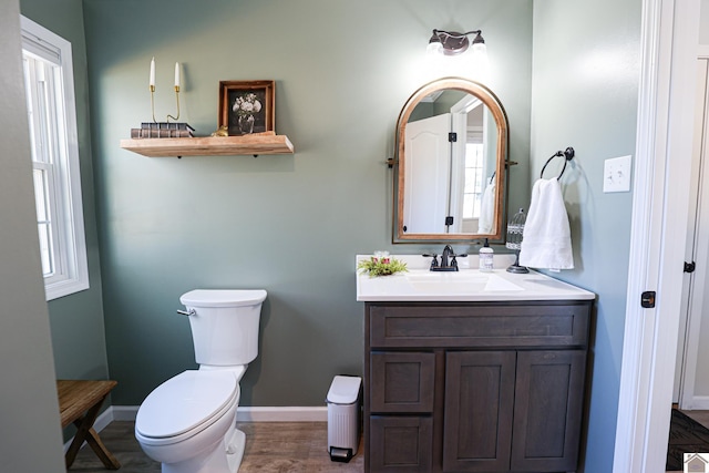 bathroom with toilet, vanity, baseboards, and wood finished floors