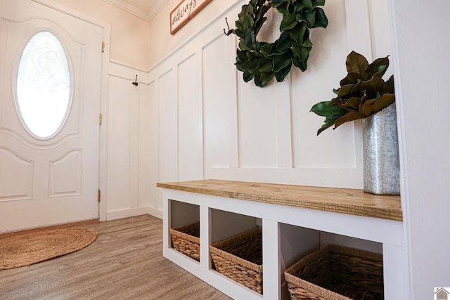 mudroom featuring light wood-style floors, crown molding, and a decorative wall