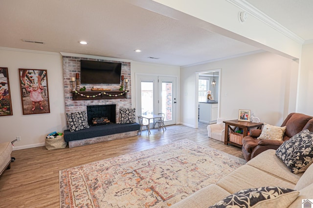 living room with wood finished floors, baseboards, visible vents, a fireplace, and crown molding