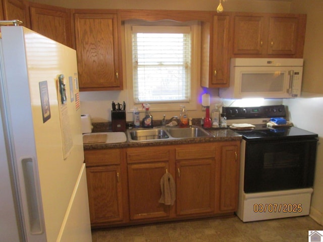 kitchen with dark countertops, brown cabinets, white appliances, and a sink