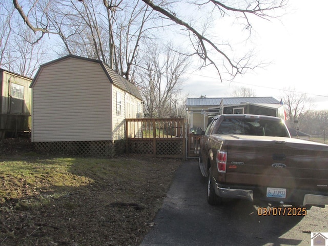 view of property exterior with a shed, a gambrel roof, metal roof, an outdoor structure, and a deck