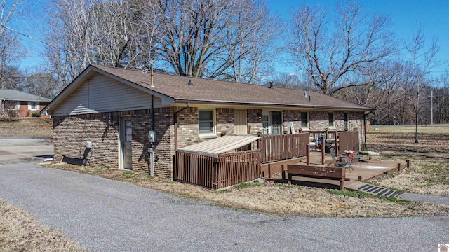 single story home featuring a deck, brick siding, and roof with shingles