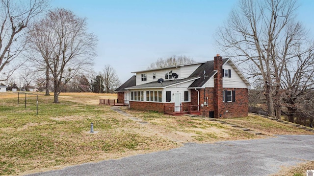 view of front facade with brick siding, a chimney, and a front lawn