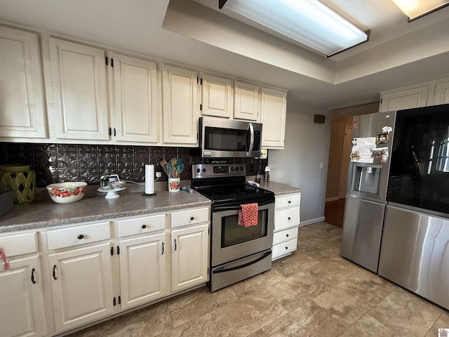 kitchen featuring baseboards, white cabinets, appliances with stainless steel finishes, a raised ceiling, and tasteful backsplash