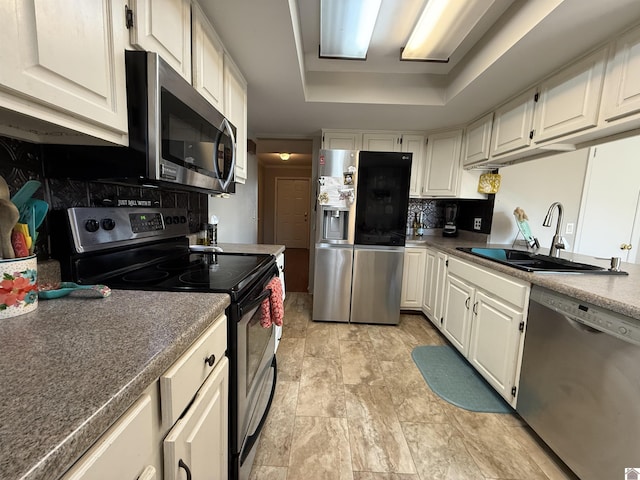 kitchen with a tray ceiling, a sink, white cabinets, appliances with stainless steel finishes, and tasteful backsplash