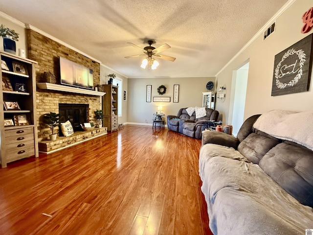 living room featuring a textured ceiling, a brick fireplace, wood finished floors, and ornamental molding