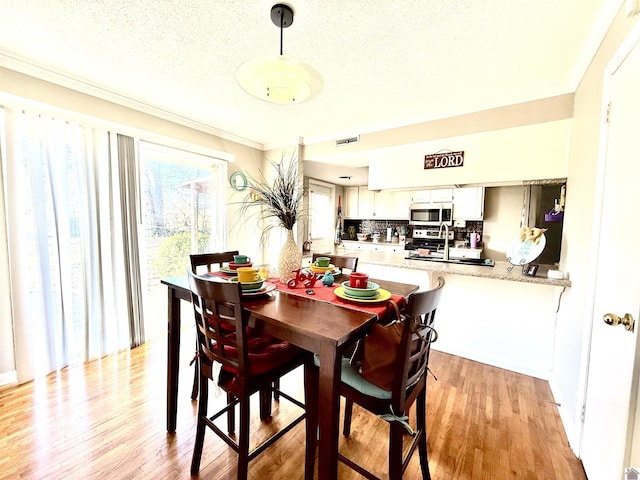 dining area featuring light wood-style flooring, visible vents, and a textured ceiling