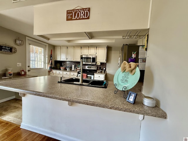 kitchen with backsplash, a peninsula, a kitchen breakfast bar, stainless steel appliances, and a sink