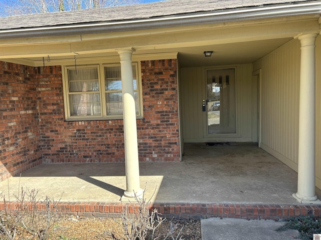 entrance to property featuring brick siding and roof with shingles