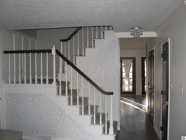 staircase featuring a textured ceiling, wood finished floors, and ornamental molding