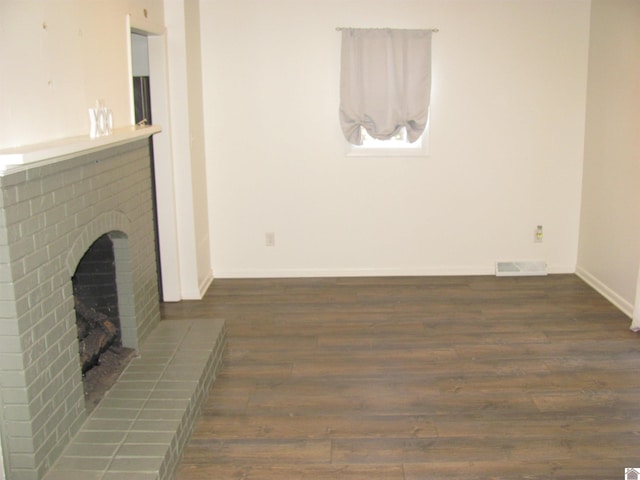 unfurnished living room with visible vents, baseboards, a brick fireplace, and wood finished floors