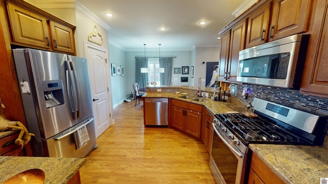 kitchen with ornamental molding, light wood-style flooring, appliances with stainless steel finishes, a peninsula, and a sink