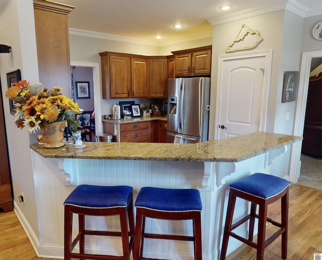 kitchen featuring a kitchen breakfast bar, light stone counters, stainless steel fridge with ice dispenser, and light wood finished floors