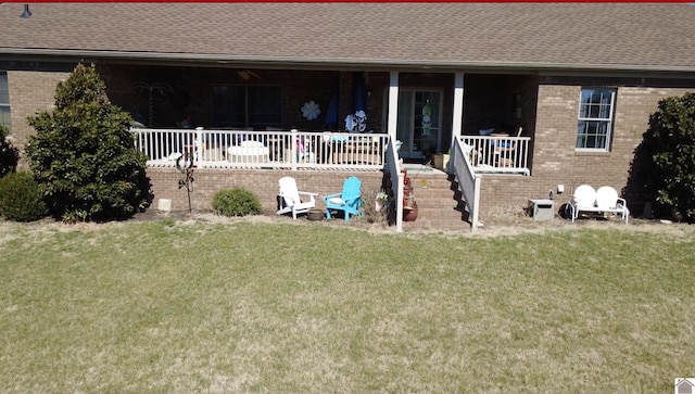 rear view of house featuring a shingled roof, brick siding, covered porch, and a lawn