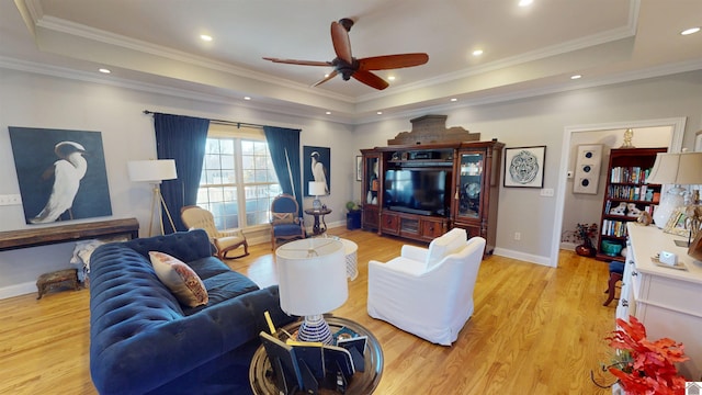 living room with a tray ceiling, recessed lighting, light wood-style floors, and ornamental molding