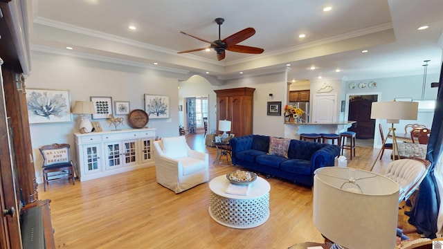 living room featuring a raised ceiling, recessed lighting, light wood-style floors, and arched walkways