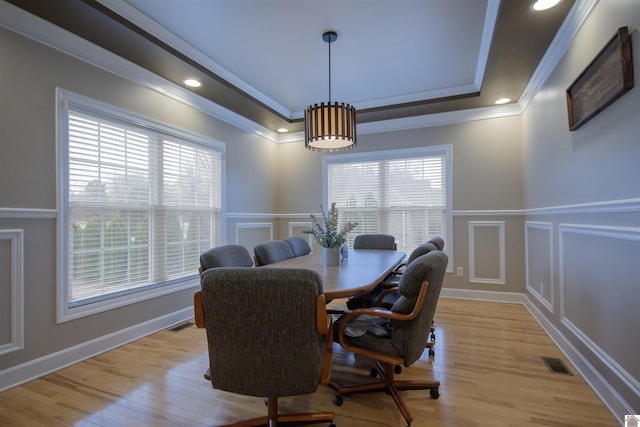 dining space with a tray ceiling, light wood-style floors, ornamental molding, and a decorative wall