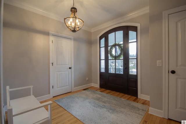 entryway with crown molding, baseboards, a chandelier, light wood-style floors, and arched walkways