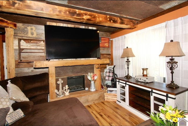 living area featuring a glass covered fireplace, beam ceiling, and wood finished floors