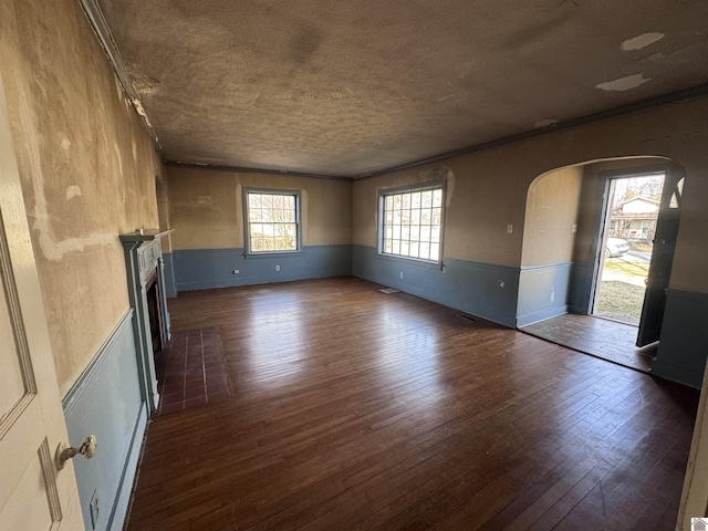 spare room with a fireplace with flush hearth, wainscoting, arched walkways, dark wood-style floors, and a textured ceiling