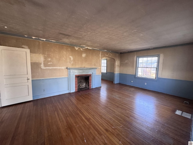 unfurnished living room featuring a wainscoted wall, arched walkways, and wood-type flooring