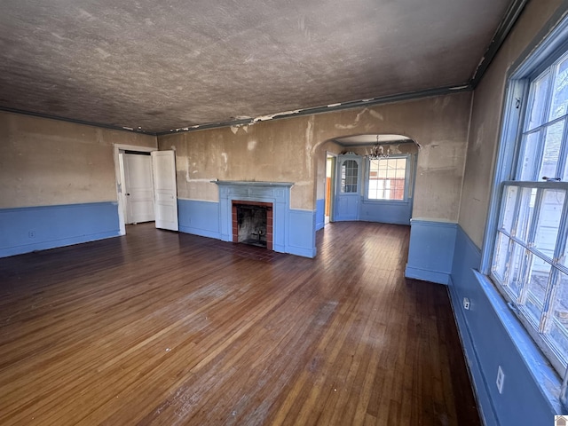 unfurnished living room featuring a fireplace with flush hearth, a wainscoted wall, an inviting chandelier, hardwood / wood-style flooring, and arched walkways