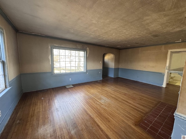 empty room featuring arched walkways, a wainscoted wall, visible vents, and hardwood / wood-style flooring