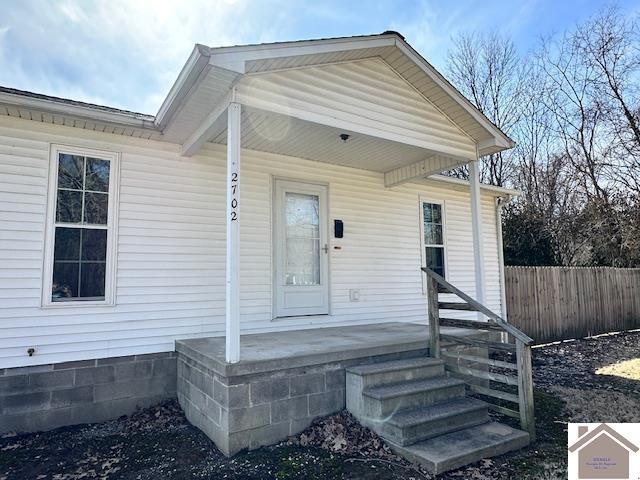 view of exterior entry with covered porch and fence