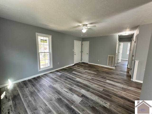 empty room with visible vents, baseboards, dark wood finished floors, a textured ceiling, and a ceiling fan