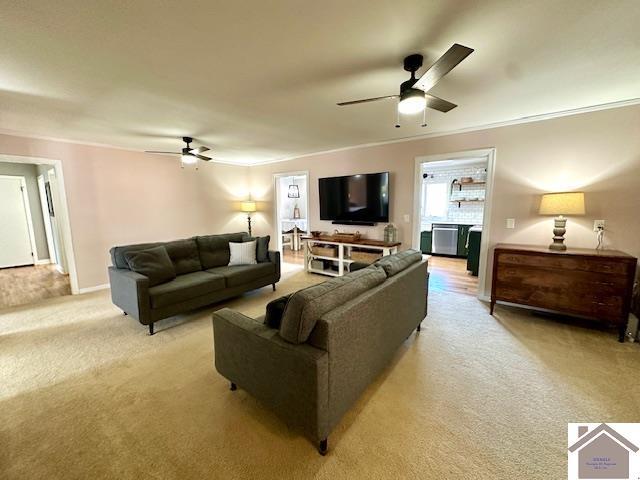 living area with ceiling fan, light colored carpet, and ornamental molding