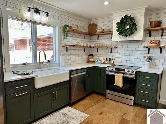 kitchen featuring open shelves, a sink, appliances with stainless steel finishes, green cabinets, and light countertops