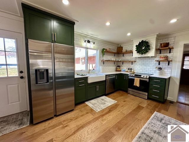 kitchen with open shelves, green cabinetry, appliances with stainless steel finishes, and a sink