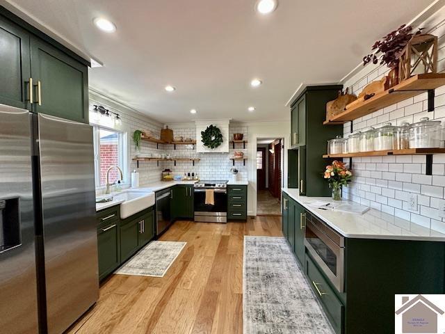 kitchen with open shelves, a sink, stainless steel appliances, green cabinets, and light countertops