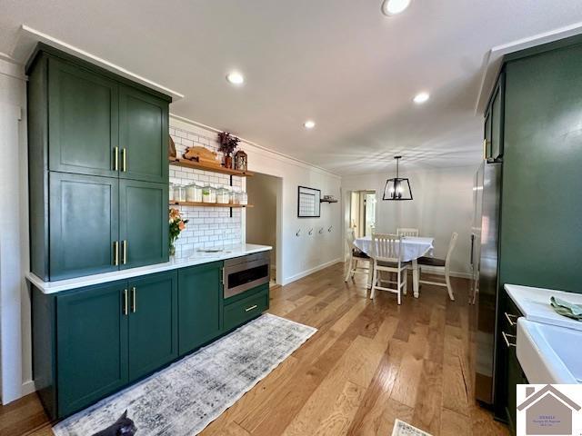 kitchen with tasteful backsplash, light countertops, light wood-type flooring, recessed lighting, and green cabinetry