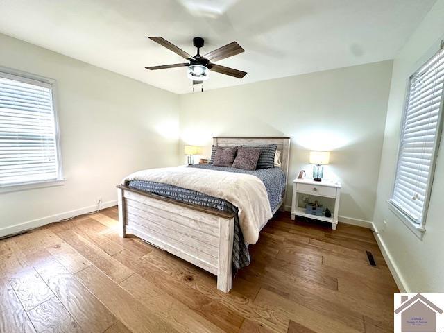 bedroom with hardwood / wood-style floors, baseboards, visible vents, and a ceiling fan