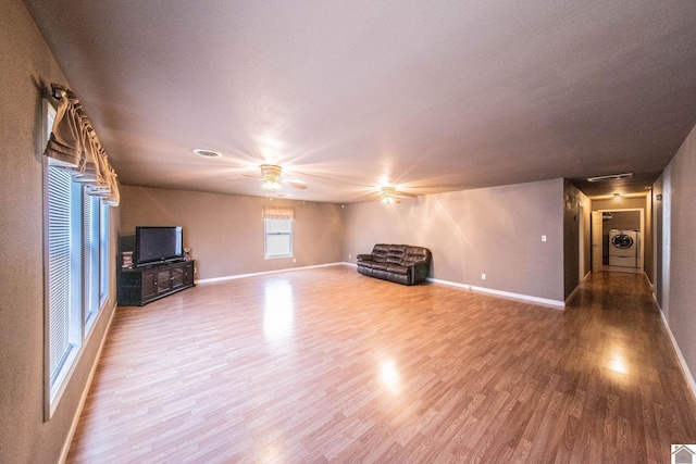 unfurnished living room with separate washer and dryer, baseboards, a ceiling fan, and wood finished floors