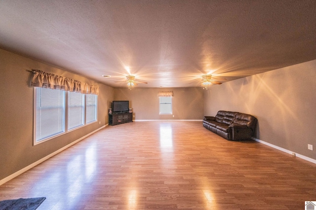 unfurnished room with a textured ceiling, wood finished floors, baseboards, and ceiling fan